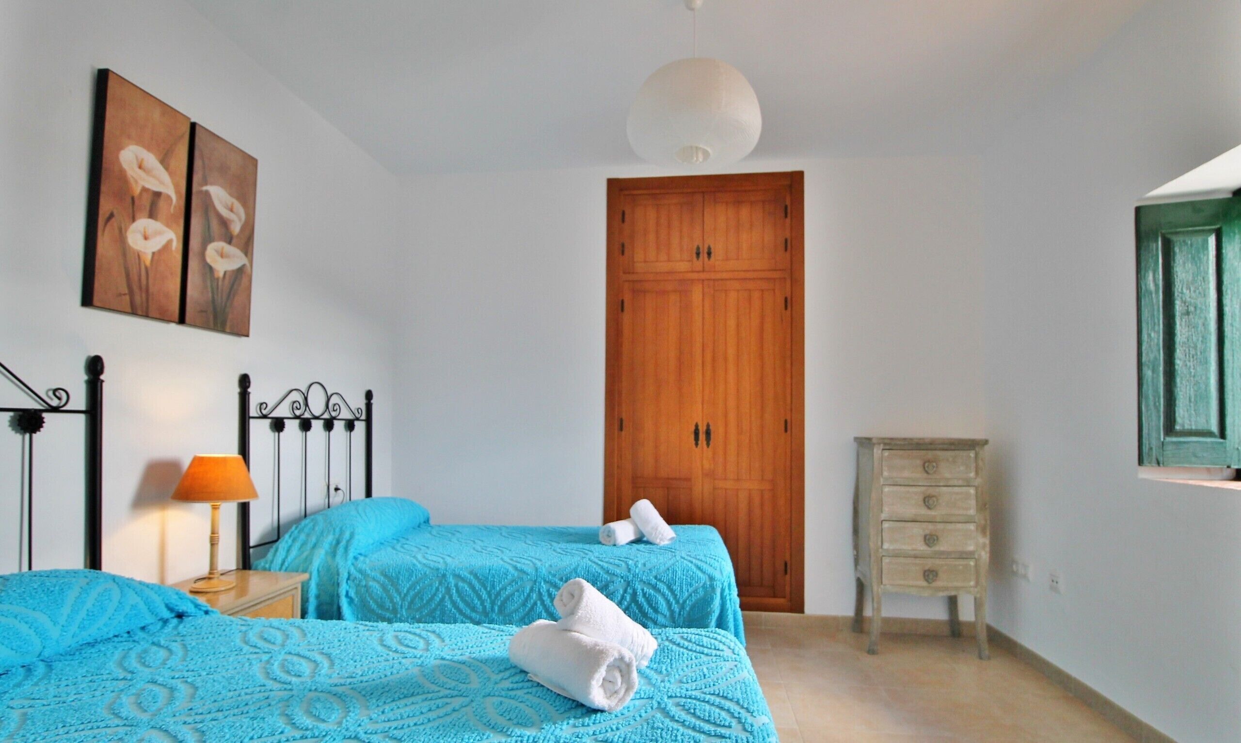 Ein Schlafzimmer mit zwei Betten, einem Holzschrank, einem Nachttisch mit Lampe und einer Kommode.