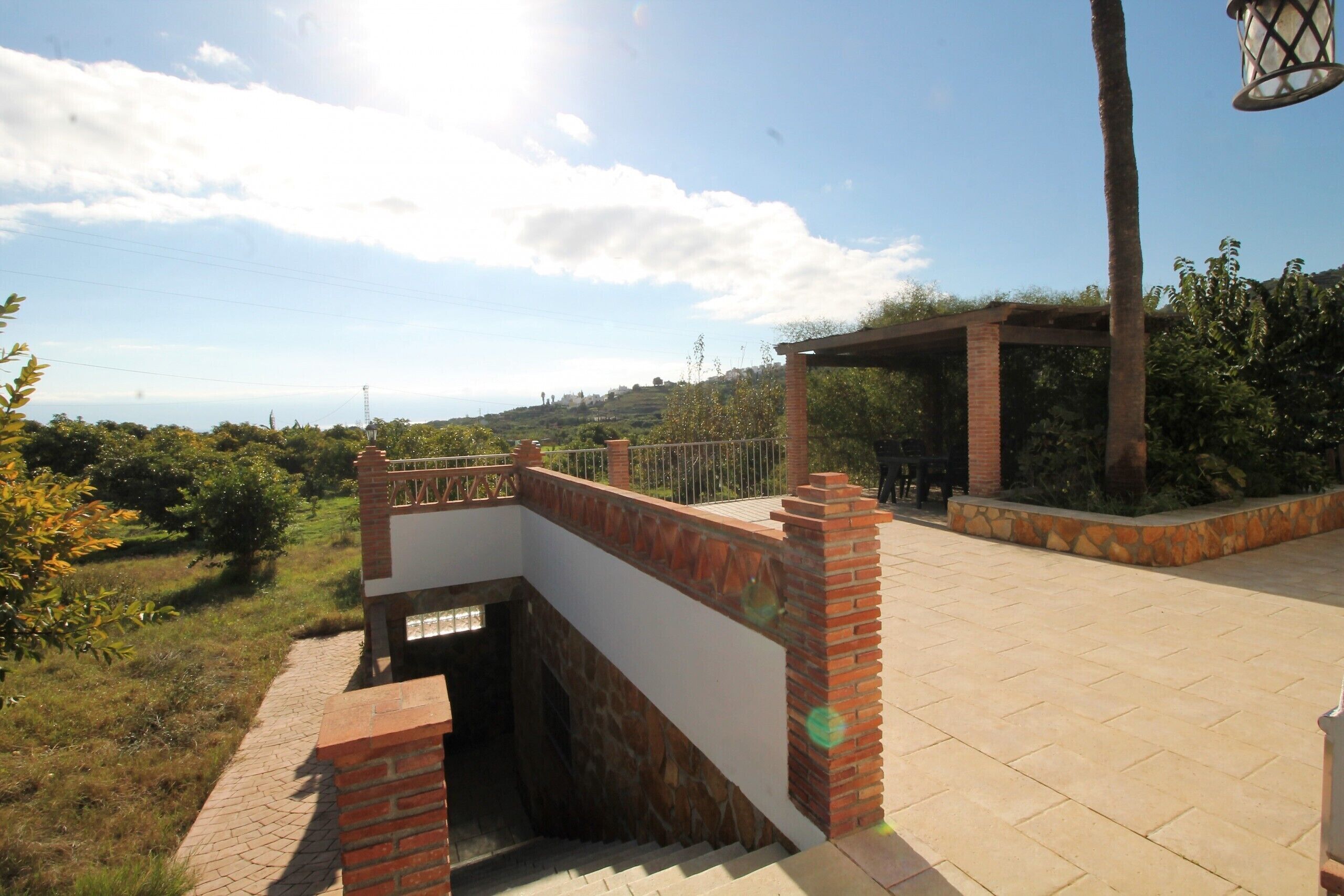 A covered outdoor area with a brick wall and a metal railing overlooking a hilly landscape.