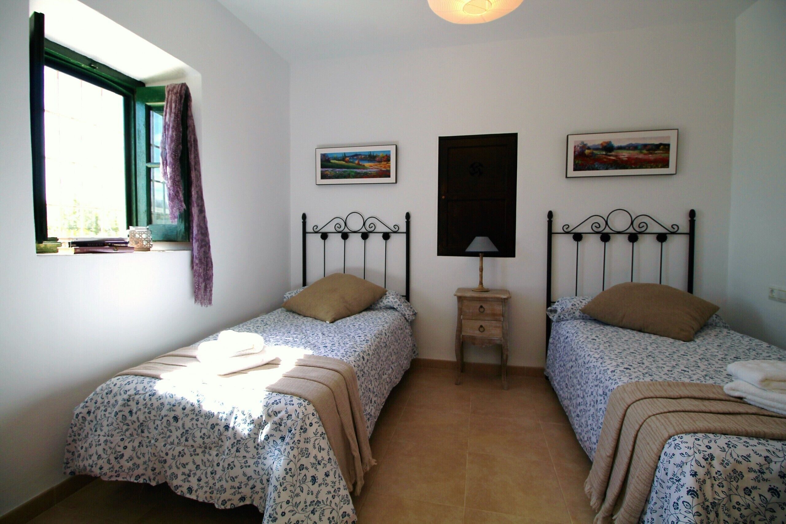 Un dormitorio con dos camas individuales, una ventana con cortina y dos cuadros enmarcados en la pared.