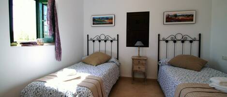 Un dormitorio con dos camas individuales, una ventana con cortina y dos cuadros enmarcados en la pared.