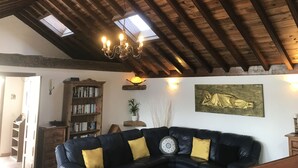 Una sala de estar acogedora con un sofá de cuero oscuro, vigas de madera en el techo, una araña y una estatua de Buda en la pared.