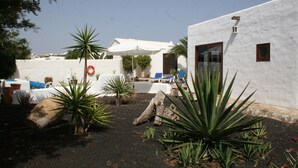 Un patio con paredes blancas, una piscina y sillones de descanso.
