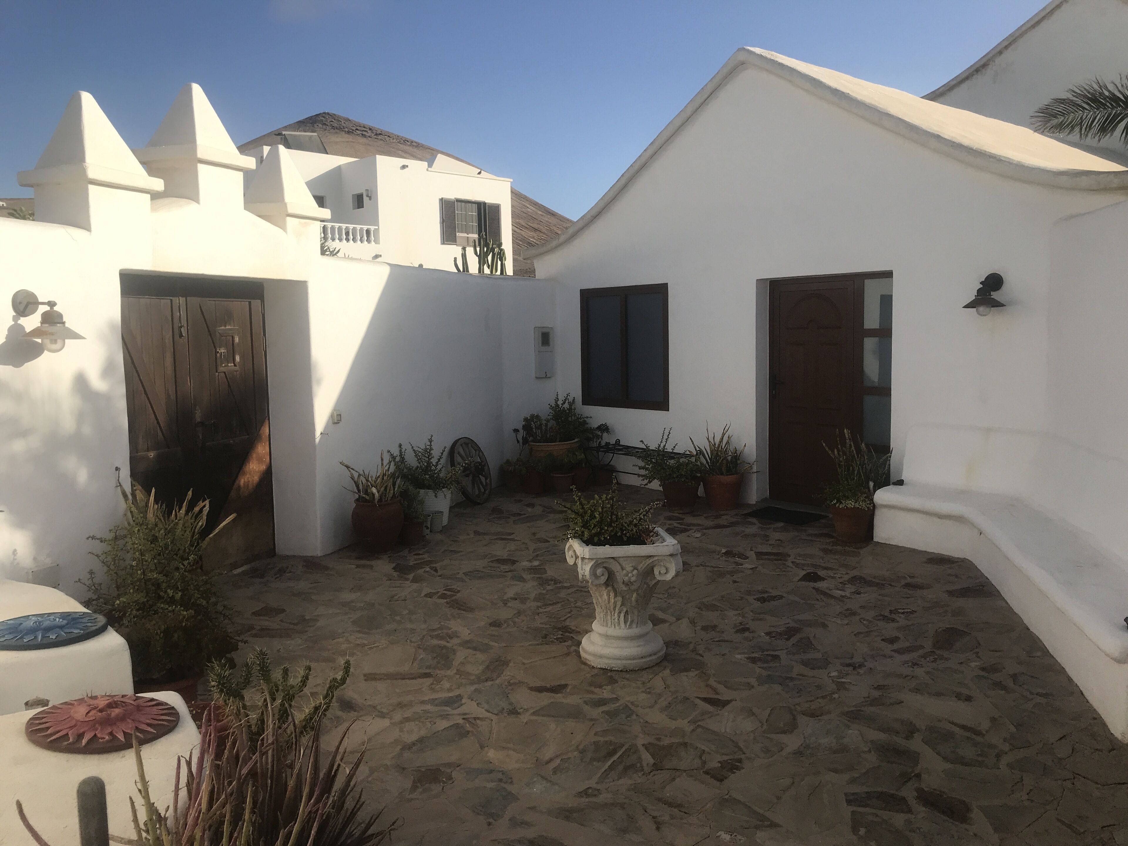 A courtyard with white walls, a stone floor, and potted plants.