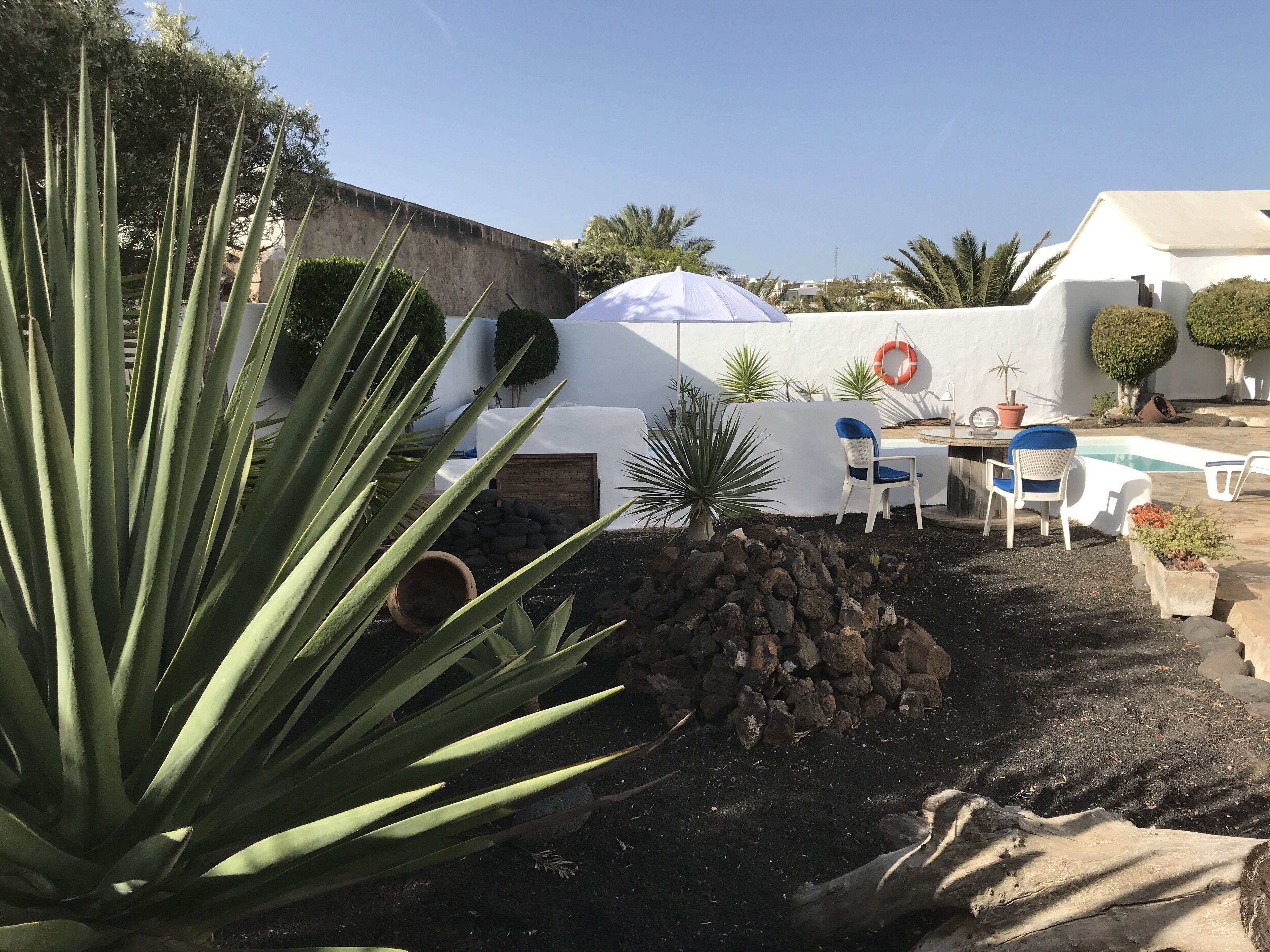 Un patio con sillas y mesa blancos, una piscina pequeña y un muro blanco con un flotador.