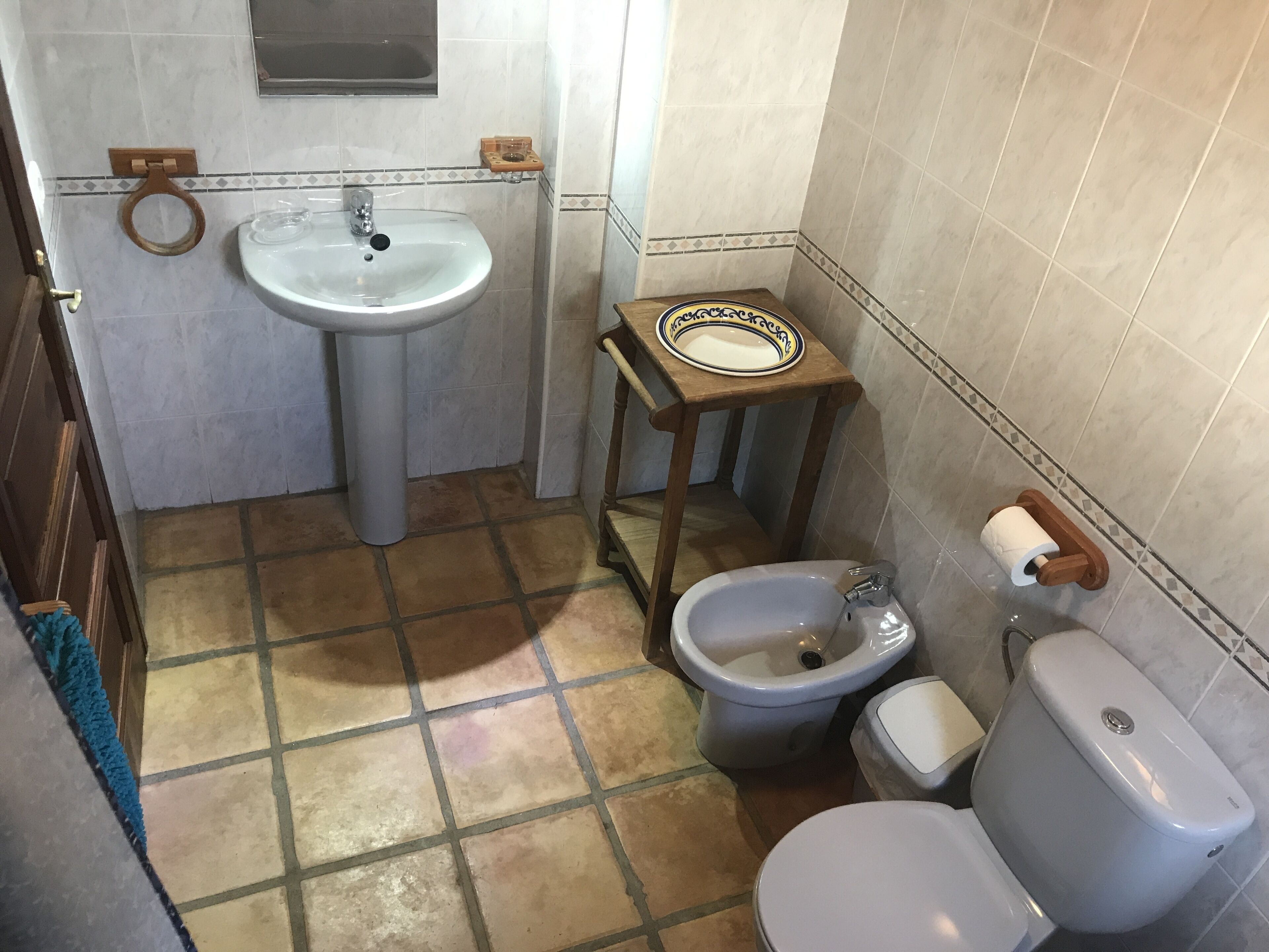 A bathroom with a sink, toilet, bidet, and a small wooden table with a plate.