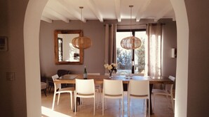 Un coin repas avec une table en bois et des chaises blanches, un miroir au mur et un luminaire suspendu.