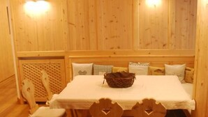 Uma área de refeições de madeira com uma mesa, cadeiras, um cesto sobre a mesa e um banco com almofadas.