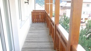 Um deck de madeira com guarda-corpo, um banco e vista para prédios e árvores ao fundo.