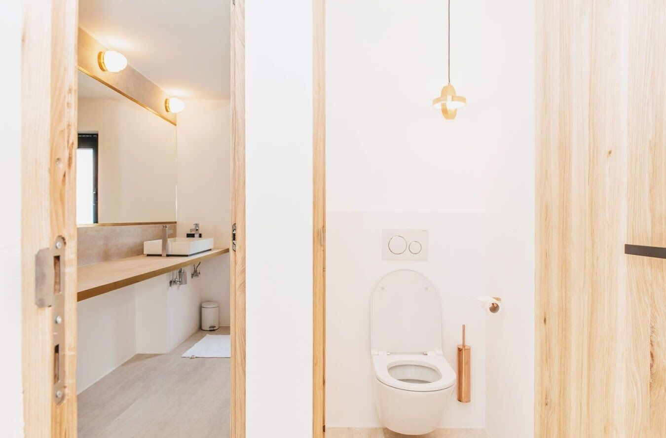 A modern bathroom with a wooden vanity, a toilet, and a hanging light fixture.