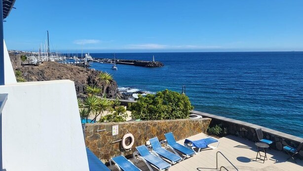 A coastal view with a stone wall, lounge chairs, and a clear blue sky. - A Wonderful Frontline Villa to Watch the Boats Go By! (Yaiza)