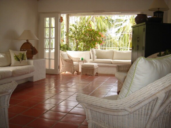 Un salón amplio con un conjunto de sofá blanco, sillones de mimbre y suelo de baldosas.