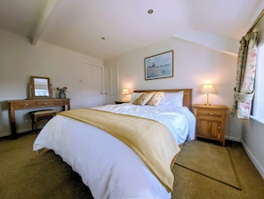 Ein Schlafzimmer mit einem großen Bett, zwei Nachttischen mit Lampen, einem Holztisch, einer Bank und einer Tür.