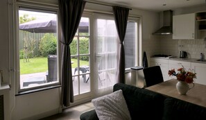A modern kitchen with white cabinets, a dining area with a table and chairs, and large sliding glass doors leading to a garden. - Holiday house near the beach and dunes of Callantsoog, decided on private property. (Schagerbrug)