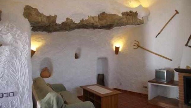 Un intérieur rustique avec un mur en pierre, une table en bois, un canapé et un téléviseur posé sur un meuble.