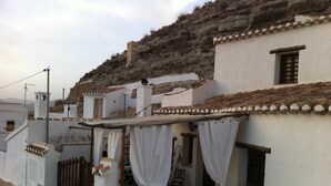 Un bâtiment traditionnel de couleur blanche, avec un toit recouvert de tuiles, un patio abrité agrémenté de rideaux blancs et un mur en pierre.