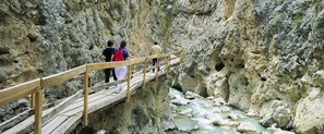 Un puente de madera con gente caminando, que lleva a un acantilado rocoso con un río abajo.