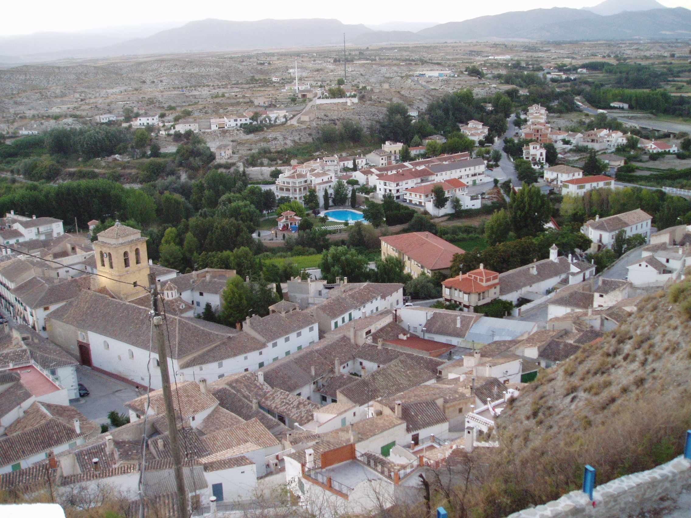 A town with white buildings, a prominent yellow tower, and a blue swimming pool.