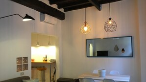 Un salon moderne avec un canapé, une table à manger et des chaises, des luminaires suspendus et un grand miroir au mur.