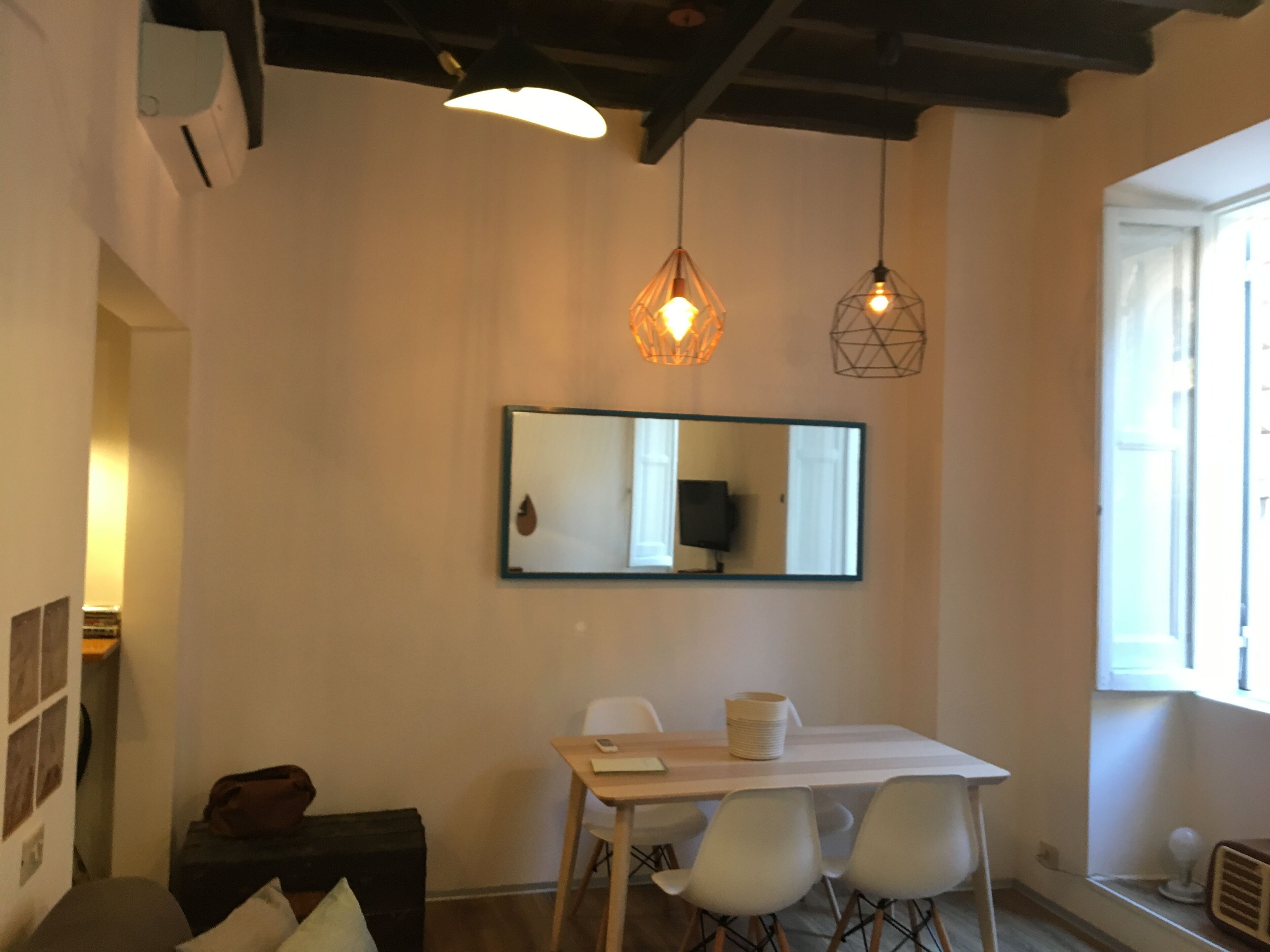 Un espace repas comprenant une table, des chaises, un miroir et des luminaires suspendus.