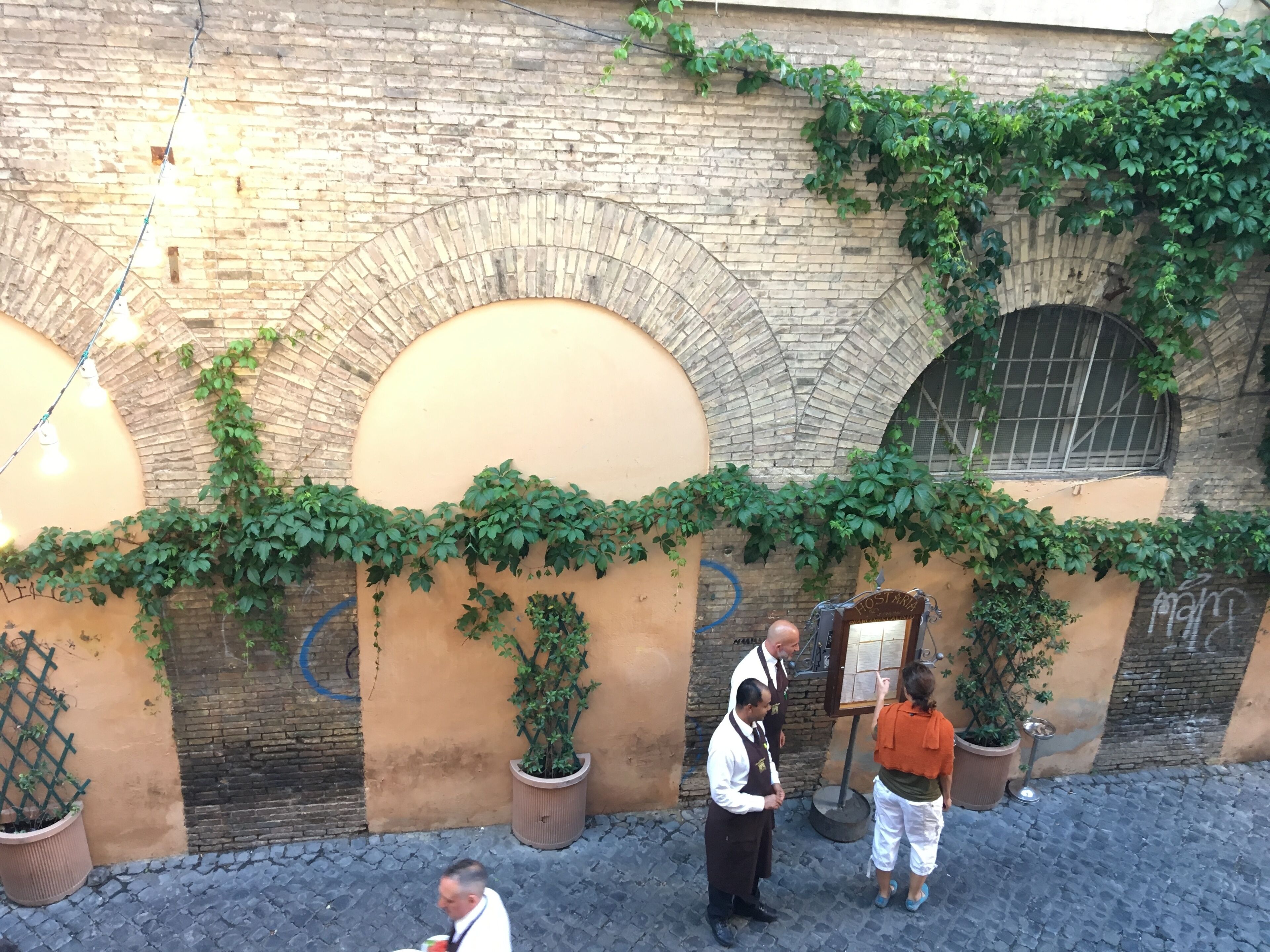 A courtyard with brick arches, potted plants, and a signboard.