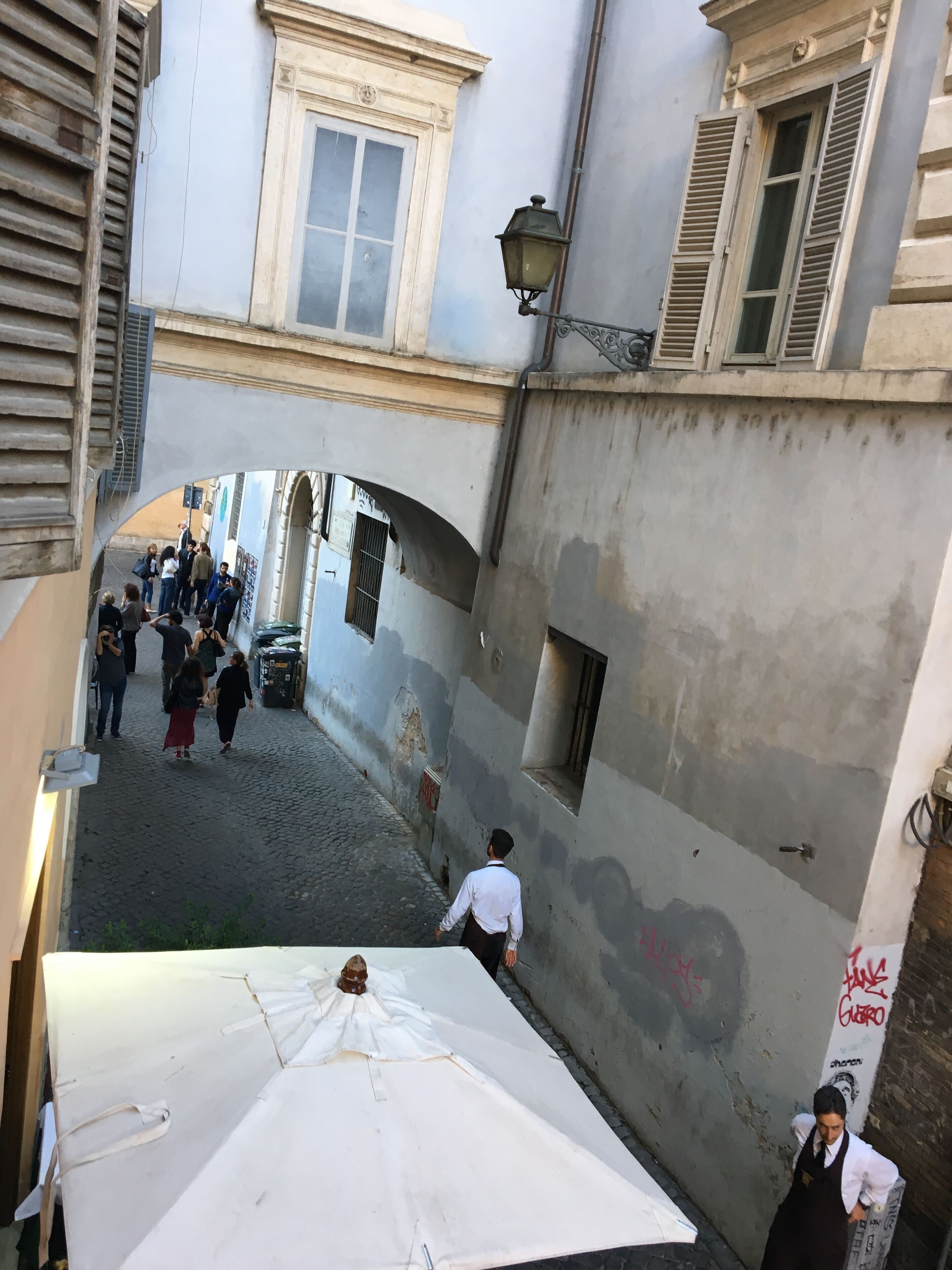 A narrow alleyway with cobblestone pavement, a white umbrella, and a group of people.
