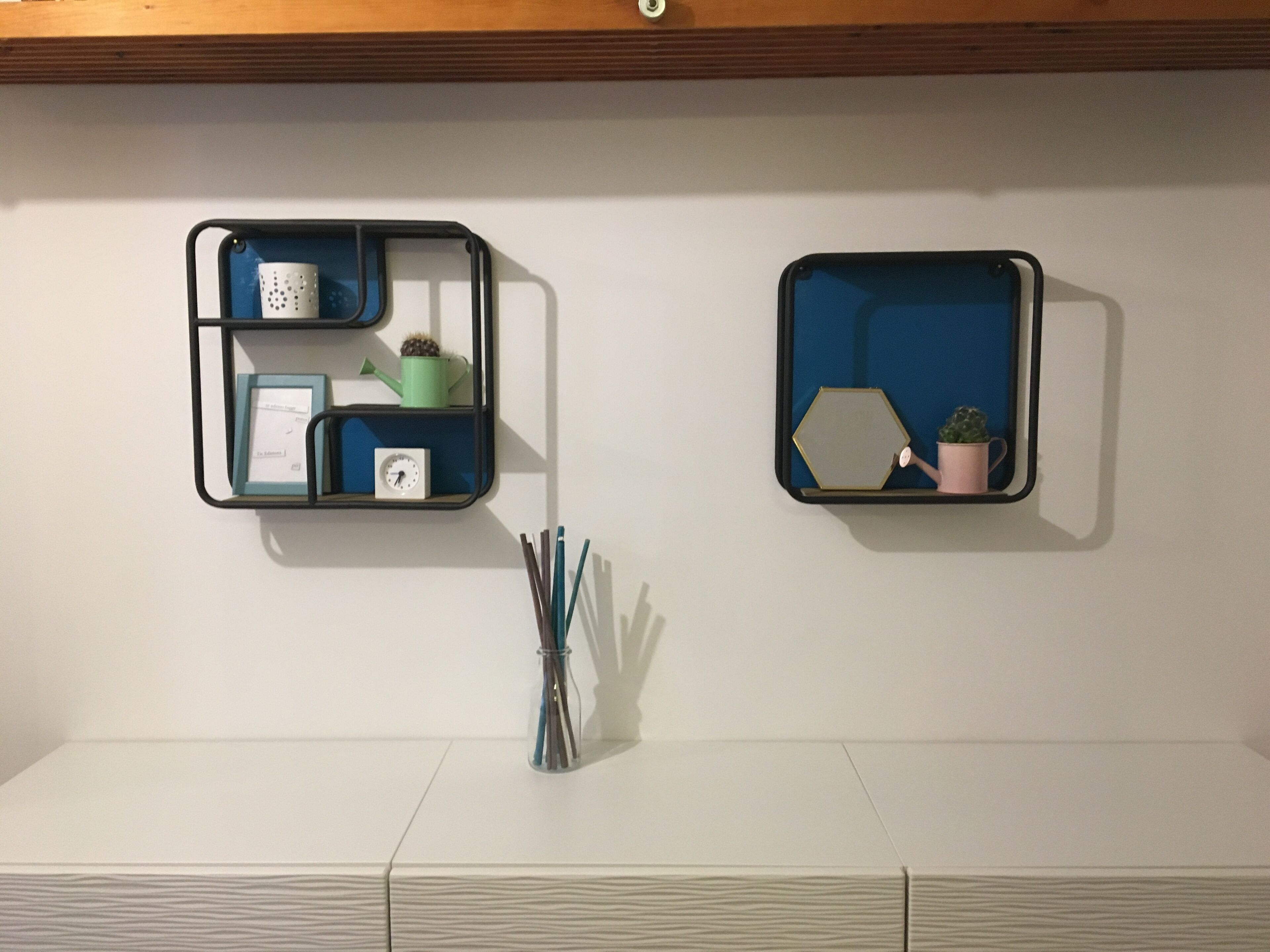 Two wall-mounted shelves with various items including a clock, a watering can, and a potted plant.