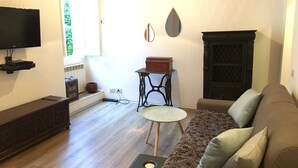Un salon comprenant un canapé, une petite table ronde, un téléviseur fixé au mur et un miroir décoratif.
