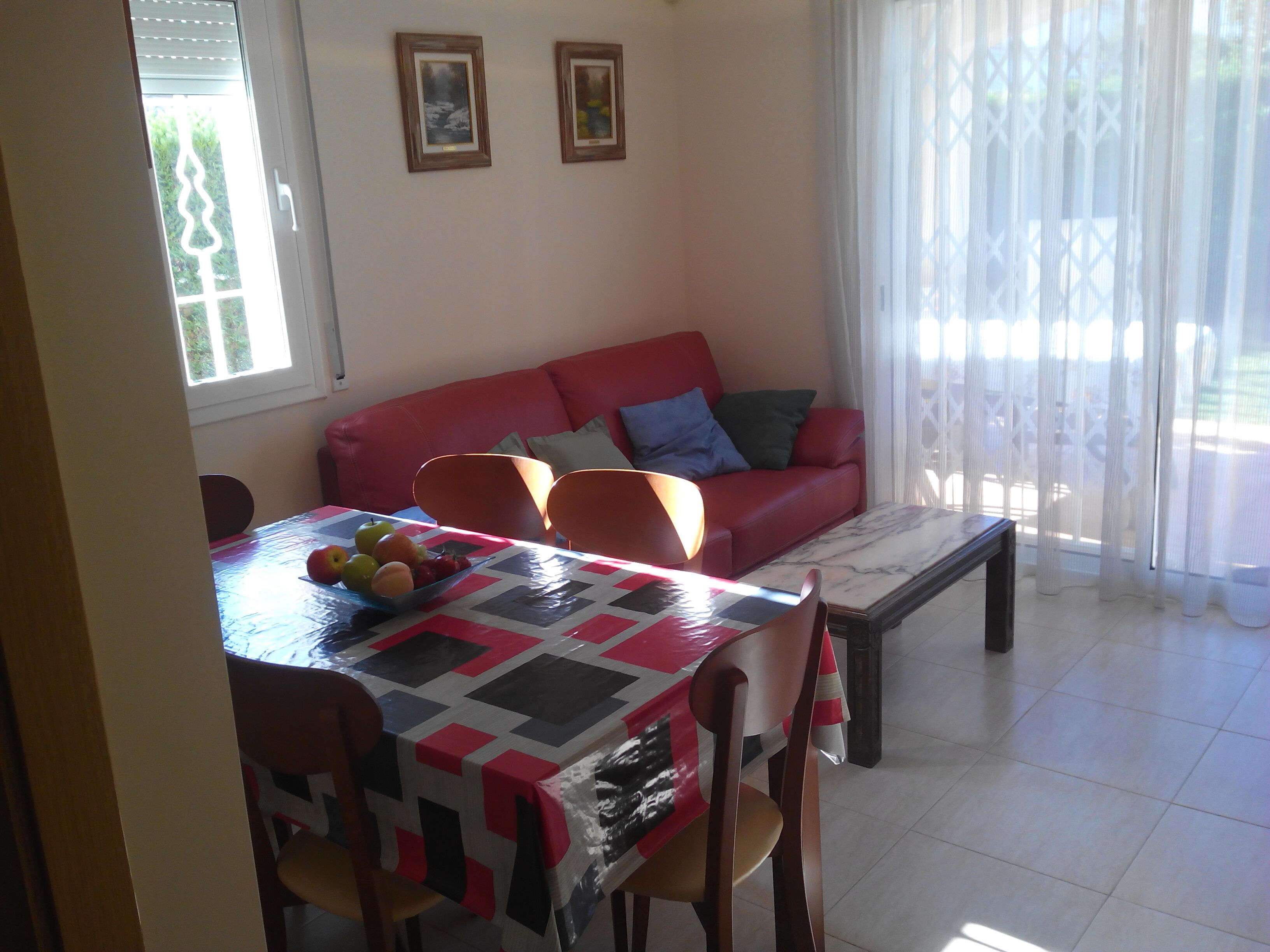 Un coin repas avec une table dressée pour quatre personnes, un canapé rouge agrémenté de coussins et deux tableaux encadrés accrochés au mur.