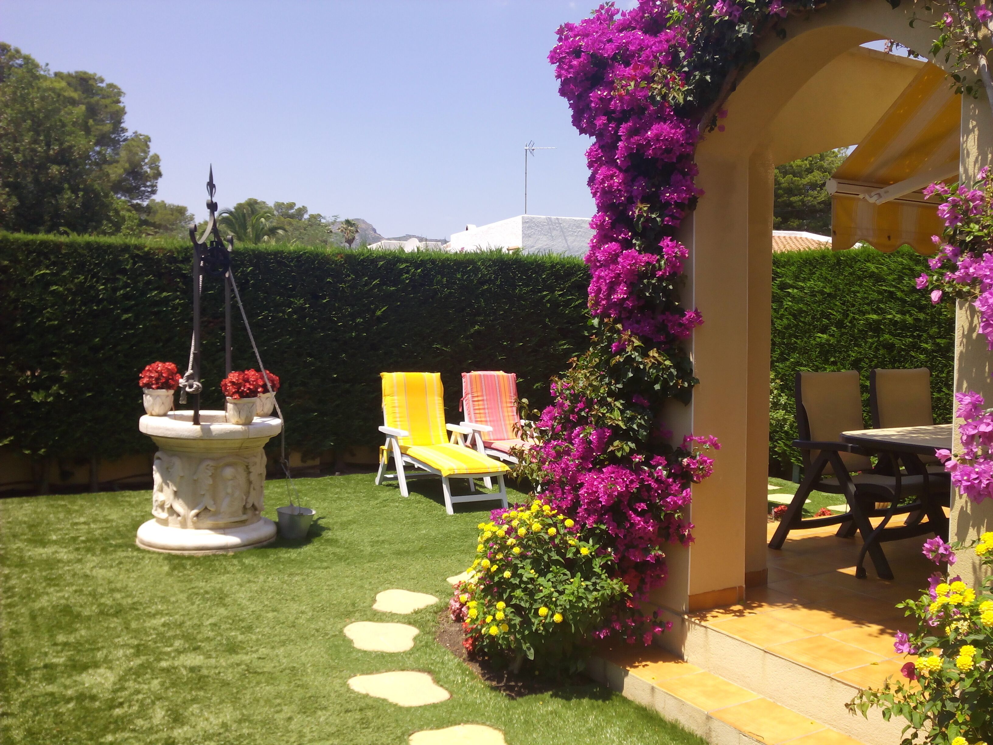 A patio area with a fountain, chairs, and a pergola covered in flowers.