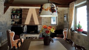 Ein rustikaler Essbereich mit Holztisch, Stühlen, Kamin und einer Pendelleuchte.