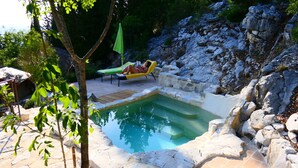 Ein Pool mit Steinbordur, eine Liege und eine Person, die entspannt.