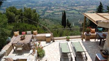 A terrace with a table and chairs, a lounge area with cushions, and a view of the countryside.