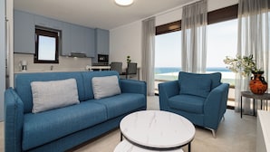 A modern living room with a blue sofa, a round coffee table, and a view of the ocean.