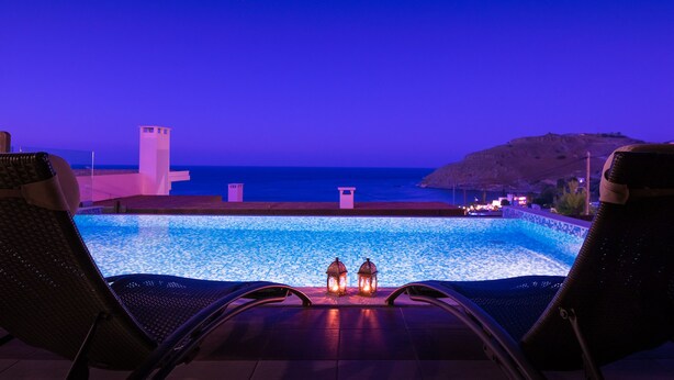 A poolside view with lounge chairs and two lanterns, overlooking a body of water and a distant structure.