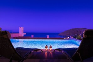 Vista sulla piscina con sedie a sdraio e due lanterne, su un'area d'acqua e una struttura in lontananza.