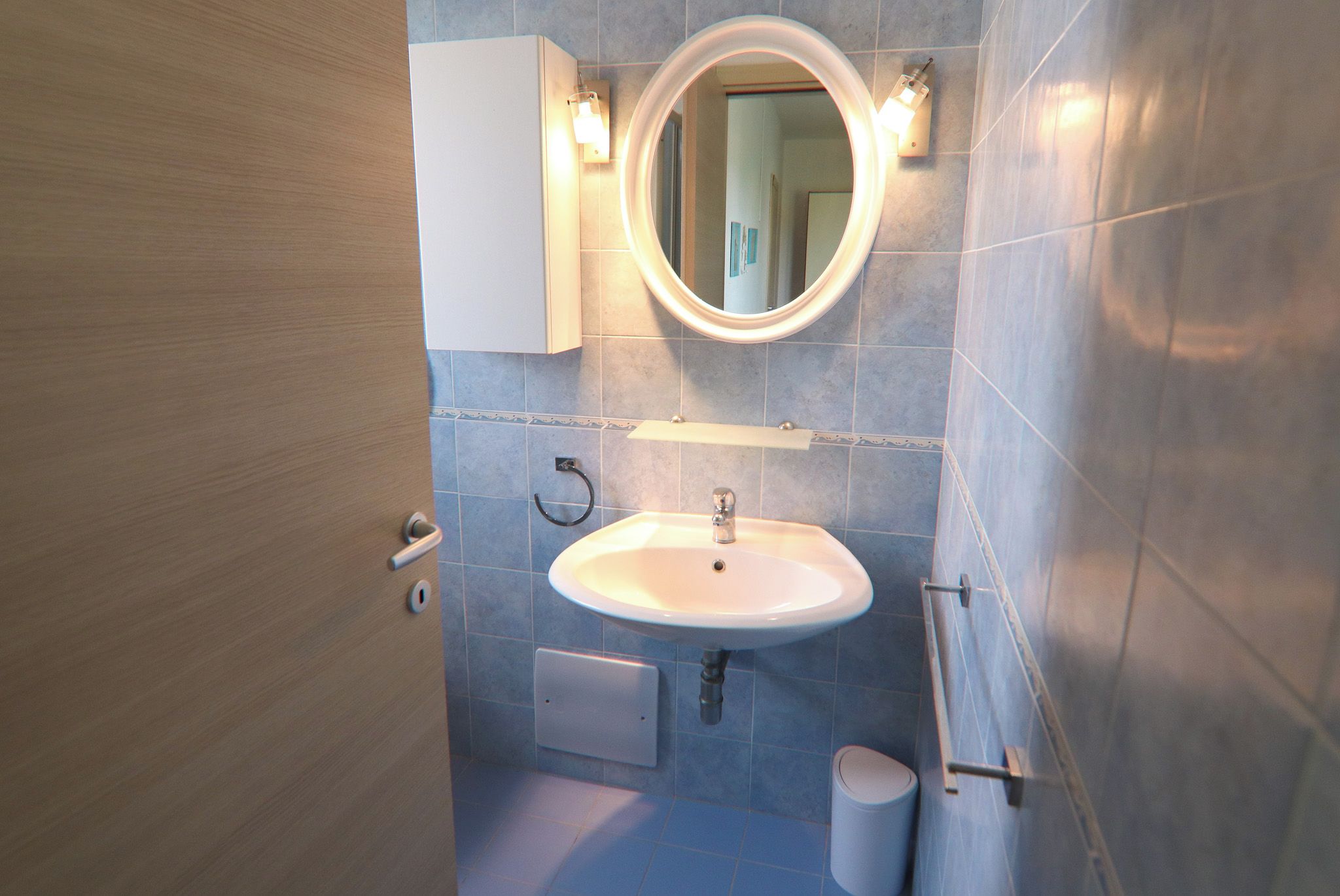 Un baño con un lavamanos blanco, un espejo con luces, un perchero y un inodoro.