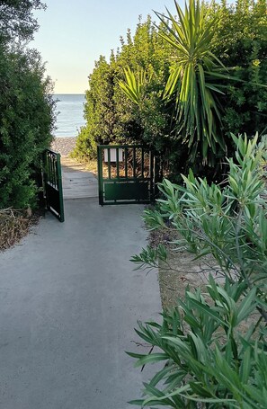 A paved pathway leading to a gated entrance with a view of the sea.