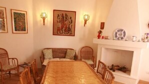 A dining area with a large wooden table surrounded by wicker chairs, a white fireplace, and wall-mounted artwork.