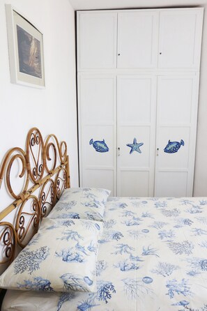 Un dormitorio con una cama, cabecera de madera, un armario blanco decorado con estrellas de mar y peces, y un cuadro en la pared.