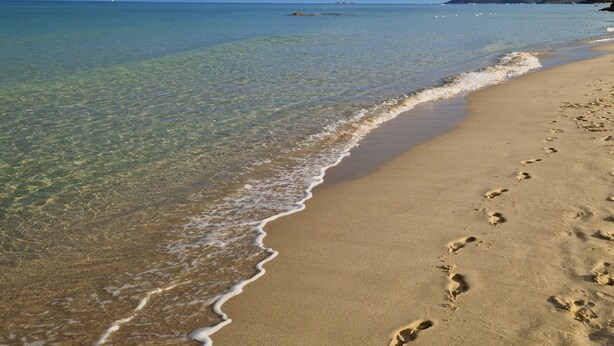 A beach with clear water, visible footprints, and distant landforms.