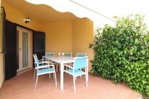 Eine Terrasse im Freien mit Tisch, Stühlen, einer Tür und einer grünen Hecke.