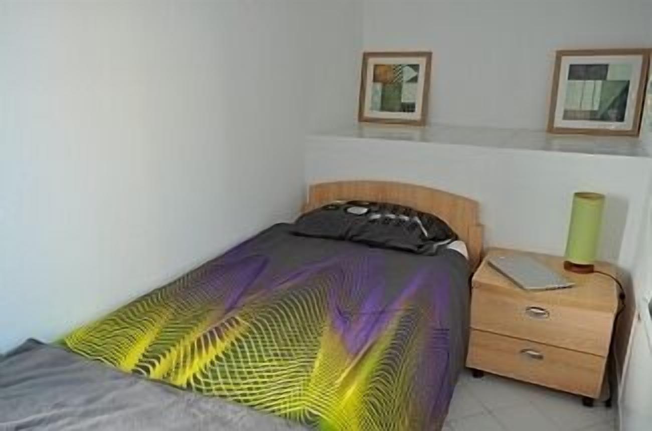Un lit simple avec une couvre-lit à motifs, une table de chevet avec une lampe et deux tableaux encadrés accrochés au mur.
