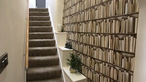 Eine Treppe mit Teppichverkleidung an der Handlaufbahn, die zu einer Zwischenebene mit Bücherregal und kleiner Topfpflanze führt.