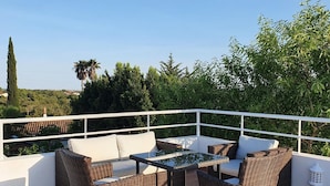 Eine Terrasse mit Korbmöbeln, einem Glastisch und Blick auf die Landschaft.