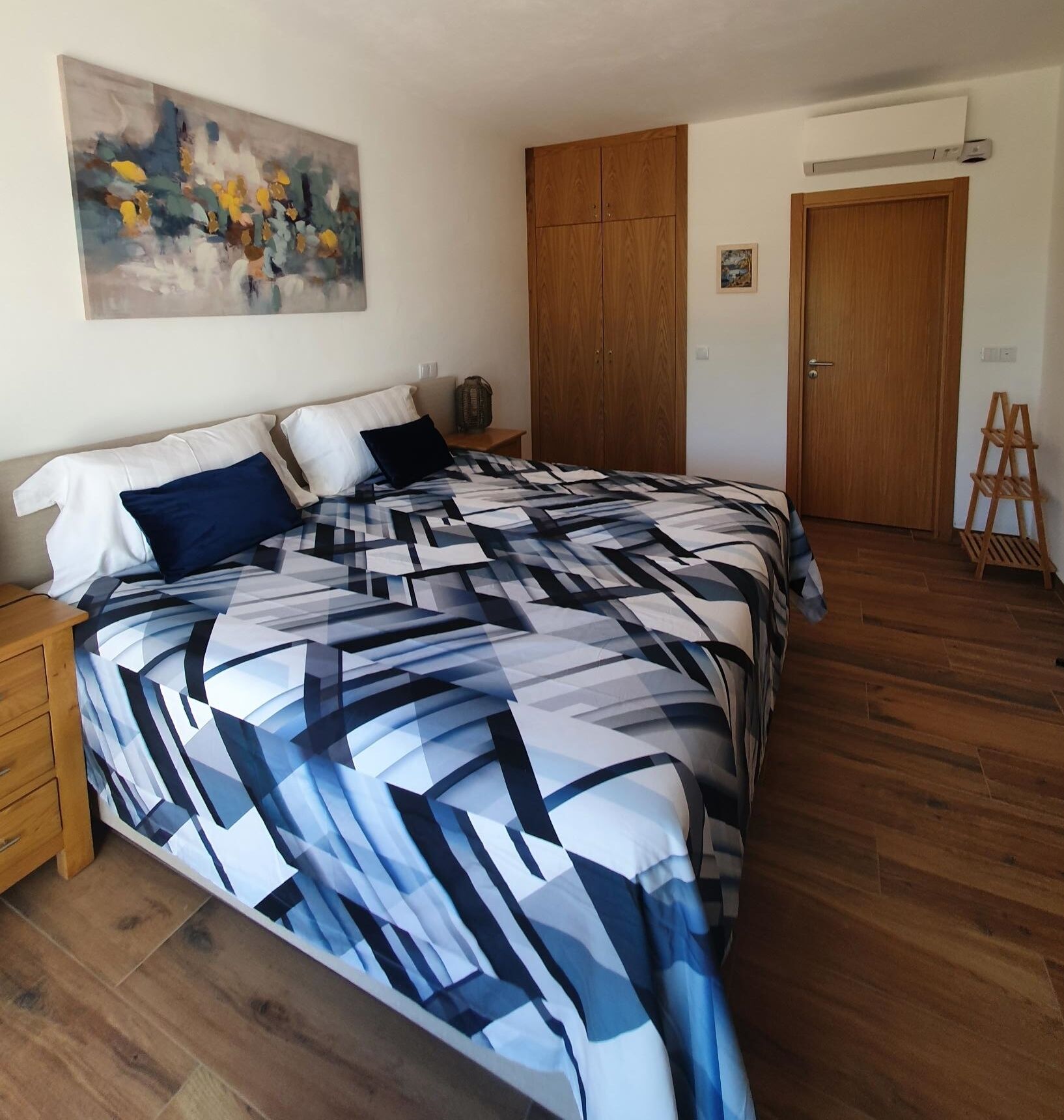 A bedroom with a bed, wooden wardrobe, and a painting on the wall.