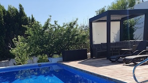 Ein Schwimmbecken mit Liegestuhl und überdachter Sitzgruppe.