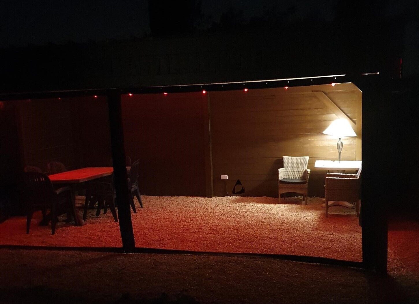 A tented outdoor area with a dining table and chairs, a lamp, and a chair with a blanket.