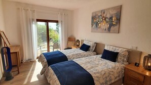 Ein Schlafzimmer mit zwei Betten, Holzboden, einem Schreibtisch und einem Fenster mit Vorhängen.