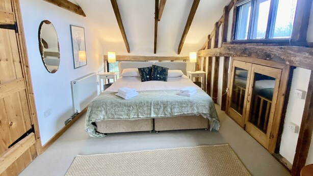 Un dormitorio con una cama grande, vigas de madera, un espejo y una ventana.