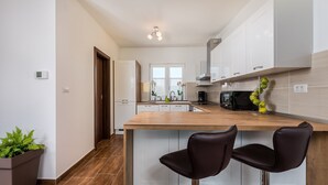 A modern kitchen with white cabinets, a wooden countertop, and two bar stools. - New Villa for 8 people with spectacular view (Potpican)